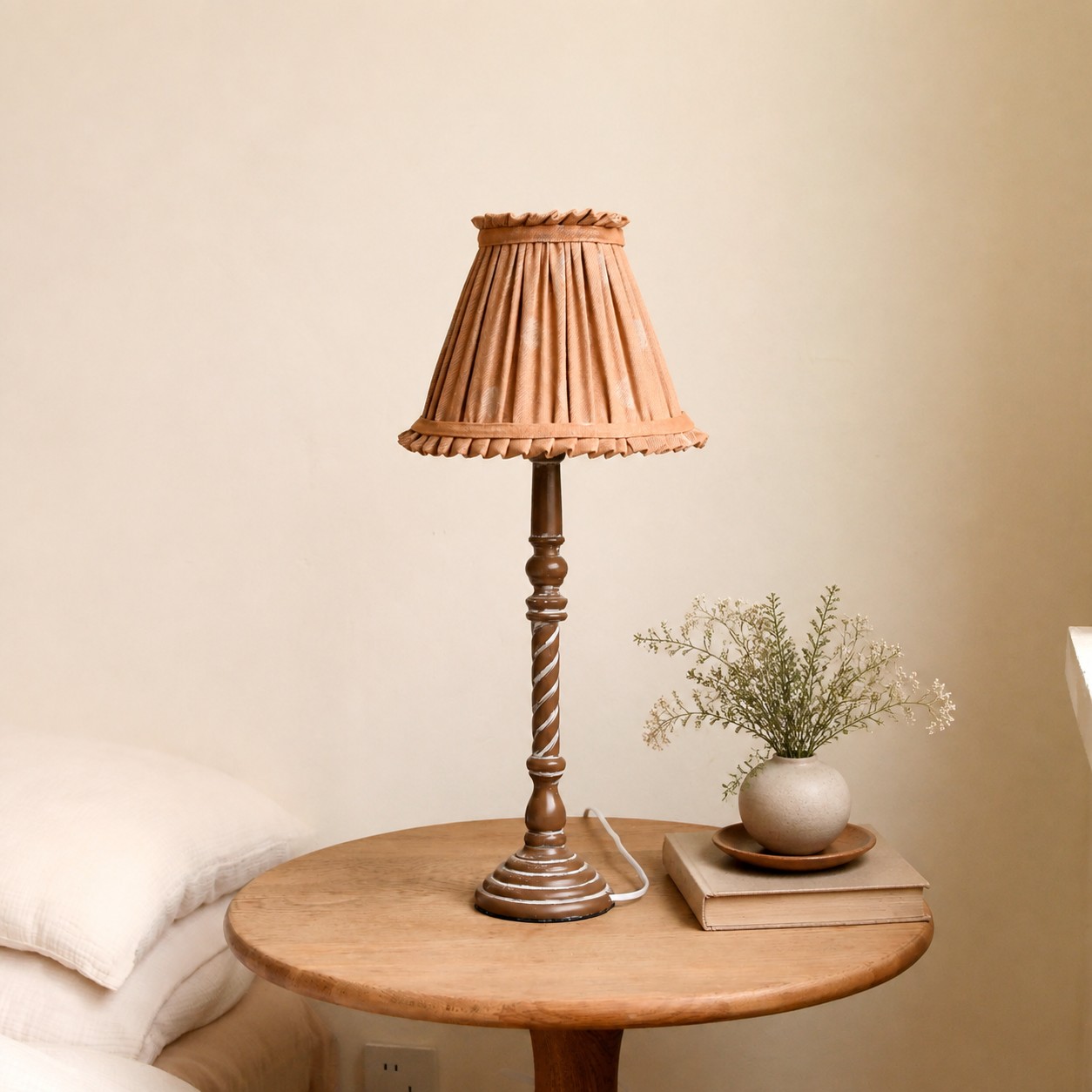 Warm tan pleated table lamp on small round bedside table
