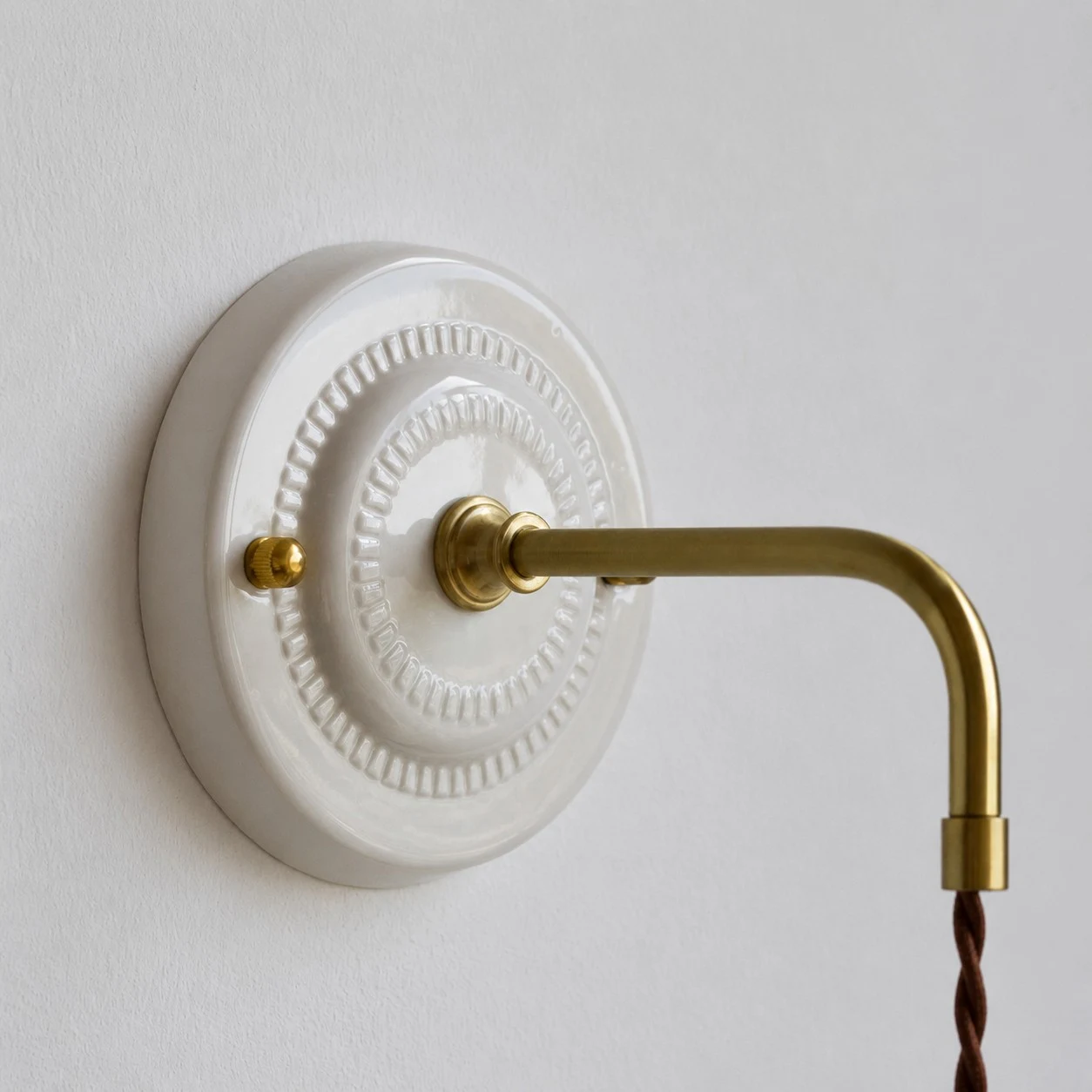 Dettaglio del piatto da parete in ceramica e del braccio della lampada color ottone
