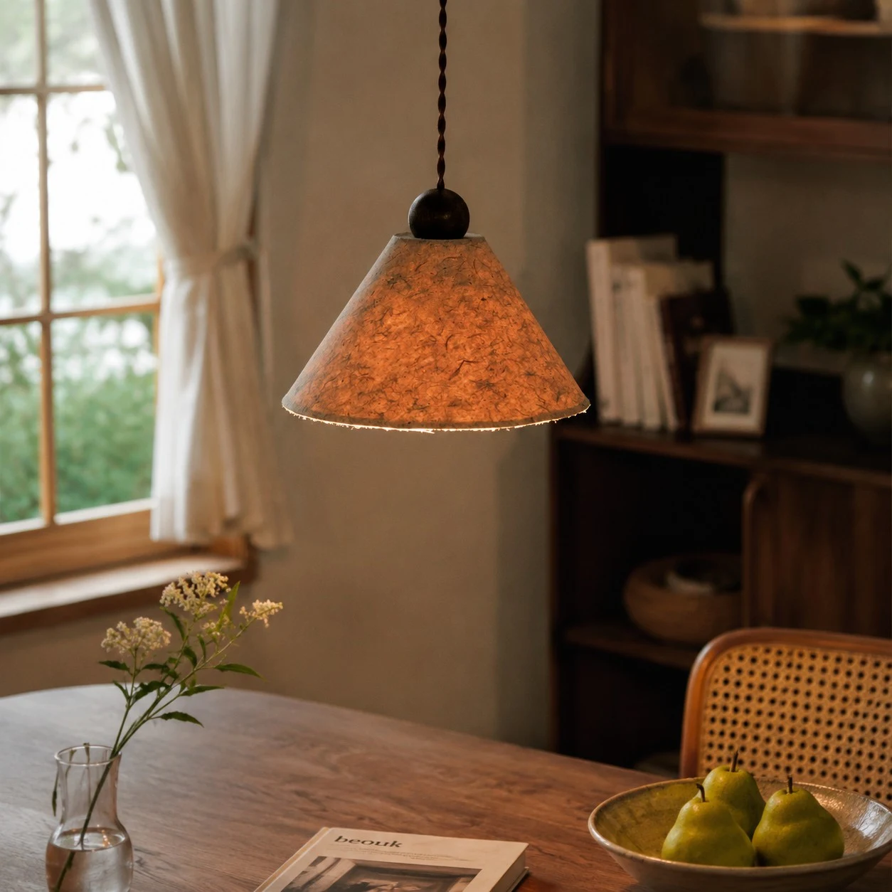 Lampada a sospensione in carta naturale dai toni caldi, installata sopra un tavolo da pranzo.